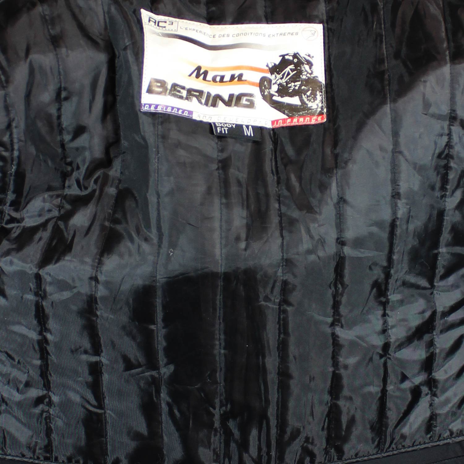A used black Bering Sting-R men's racing leather jacket in size M. In very good condition with minor scratches, it features Level 1 track protectors at the elbows, shoulders, neck, and back, a removable thermal liner, and a short connection zipper for pants.