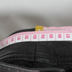 Used Damen Leathers black vintage leather pants with an adjustable leg string for fit, showing minor scratches and wrinkles from age.