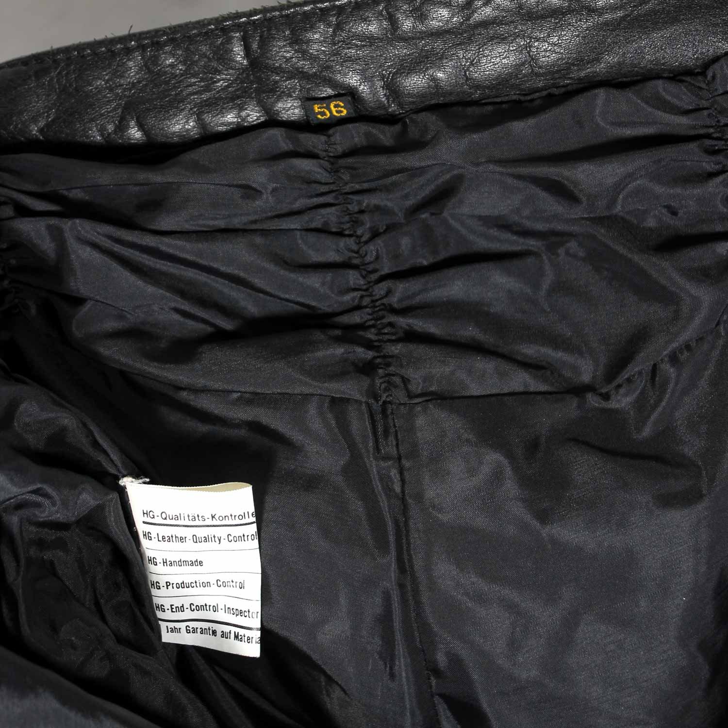 A pair of used black Hein Gericke leather pants in a vintage Café Racer style, size 56 (94 cm waist). In good condition (7.5/10) with minor use marks. Features include soft foam knee protection, an adjustable waist with a stretch panel and built-in belt, two front pockets, and a short connecting zip for a motorcycle jacket.