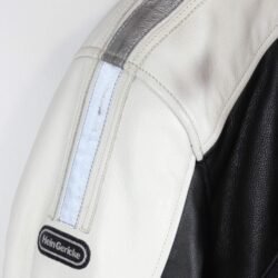 A used black and white Hein Gericke leather jacket in a women's Café-Racer style, size 44. In good condition with minor scratches, it features protection at the elbows, shoulders, and back, reflective elements, a full-length connection zipper, and a design intended to be waterproof.
