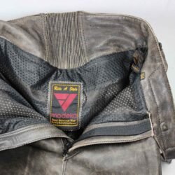 Used brown leather Modeka cafe-racer pants in size 54, featuring a stretch fit for an 82-86 cm waist. The condition is very good at 8.5/10 with only very minor surface scratches. Includes foam protectors at the knees and hips for safety. A distinctive vintage motorcycle trouser with a classic style