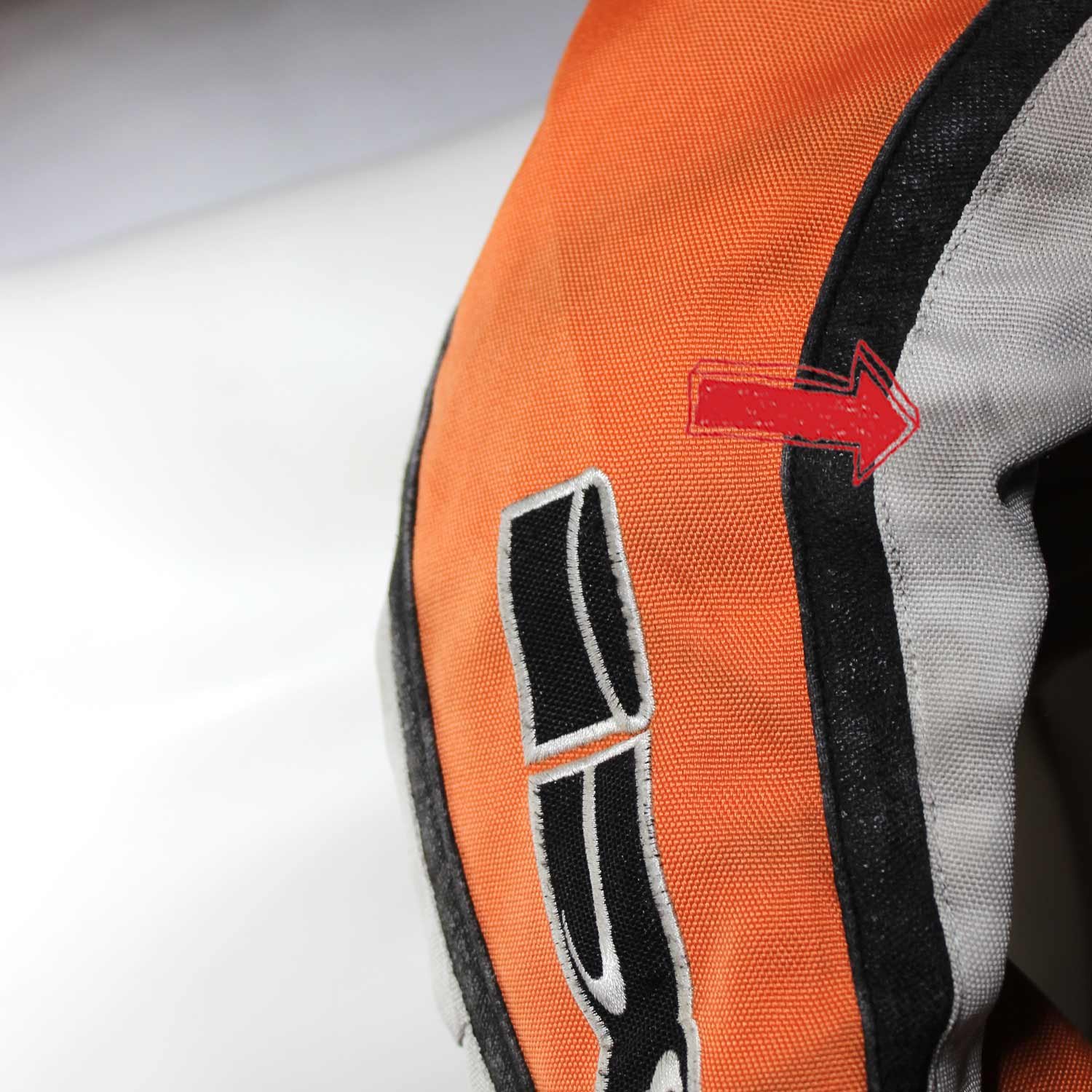A used black, orange, and crème IXS 79 Racing Team textile jacket in size L. In fair condition with some wear, pulled threads, and potential fading, it features protection at the back, shoulders, and elbows, a removable thermal liner, and a full-length connection zipper.