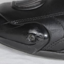 A pair of used black Gaerne G-RT racing motorcycle boots in size 43, made of leather. Features include heel, toe, gear lever, ankle, and shin protection, a non-slip oil-resistant sole, a wrap-around heel cup, and a double closure system with a zip and wide Velcro strap. Shows scratching on the plastic protectors.