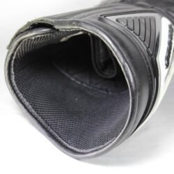 A pair of used black Gaerne G-RT racing motorcycle boots in size 43, made of leather. Features include heel, toe, gear lever, ankle, and shin protection, a non-slip oil-resistant sole, a wrap-around heel cup, and a double closure system with a zip and wide Velcro strap. Shows scratching on the plastic protectors.