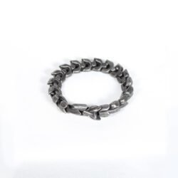 A close-up of a men's heavy metal bracelet inspired by the Nordic myth of Jormungandr. It features interlocking links resembling dragon scales, crafted from blackened stainless steel with an antique finish. The bracelet rests on a dark surface.