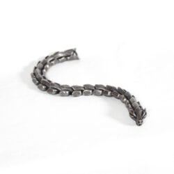 A close-up of a men's heavy metal bracelet inspired by the Nordic myth of Jormungandr. It features interlocking links resembling dragon scales, crafted from blackened stainless steel with an antique finish. The bracelet rests on a dark surface.