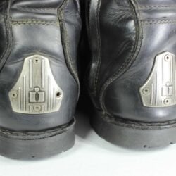 A pair of black ICON ONE THOUSAND 12" full-grain leather motorcycle boots, size 47, in good condition. Features ankle armor, reinforced shifter and shin protection, water-repellent leather, and a Goodyear welt construction. Shows typical wear, a missing screw on a back plaque, and a minor buckle flaw that does not hinder function.