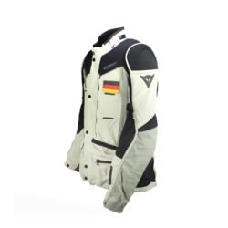 A black and beige Dainese D-Explorer adventure motorcycle jacket, size 58, in very good condition. Features an advanced modular flap system for ventilation, pockets for shoulder, elbow, and back protectors, and a removable rear exhaust vent. The jacket includes a replaceable country flag patch.